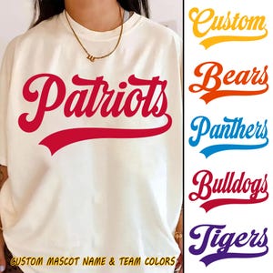 Puede incluir: Camiseta color crema con la palabra "Patriots" en escritura roja en la parte delantera. La imagen también muestra una lista de nombres y colores de equipos, incluyendo "Bears", "Panthers", "Bulldogs" y "Tigers". El texto "CUSTOM MASCOT NAME & TEAM COLORS" está en la parte inferior.