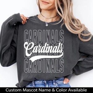 Puede incluir: Sudadera gris oscuro con la palabra "CARDINALS" apilada en blanco. La palabra "Cardinals" tambi&eacute;n est&aacute; escrita en una fuente de escritura. El texto "Custom Mascot Name & Color Available" est&aacute; en la parte inferior.