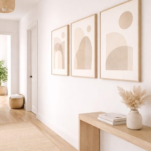 Peut inclure: Trois impressions d'art abstrait encadrées avec des formes beiges et beiges sont accrochées à un mur blanc. Une console en bois clair contient un vase de fleurs séchées et des livres. Un tapis tissé et une suspension complètent le couloir aux tons neutres.