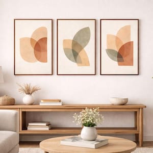 Puede incluir: Tres impresiones artísticas abstractas enmarcadas con tonos cálidos de naranja, beige y verde. La obra presenta formas geométricas superpuestas. Los marcos son de color marrón oscuro y las impresiones se exhiben en una pared blanca.