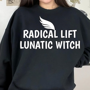 May include: Black sweatshirt with the text "RADICAL LIFT LUNATIC WITCH" in white, along with a white wing graphic. The sweatshirt is a solid black color.
