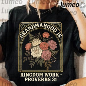 Puede incluir: Camiseta negra con un diseño floral y el texto "GRANDMAHOOD IS KINGDOM WORK - PROVERBS 31". El diseño incluye rosas en tonos rosa, melocotón y blanco, con hojas verdes, todo dentro de un marco decorativo.