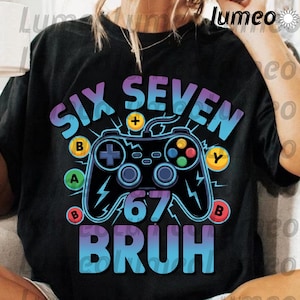 Könnte beinhalten: Schwarzes T-Shirt mit einem farbenfrohen Grafikdesign. Das Design zeigt die Wörter "SIX SEVEN BRUH" in einer Farbverlaufs-Schriftart, einen Controller und die Zahl "67". Der Controller hat die Tasten A, B und Y.