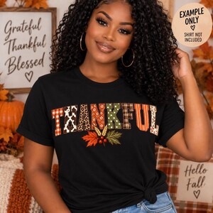 Peut inclure: Un t-shirt noir à manches courtes avec le mot THANKFUL en grandes lettres majuscules. Chaque lettre présente un motif différent, notamment à carreaux, léopard, floral et rayé. Sous le texte se trouvent trois feuilles d'automne et des baies rouges.