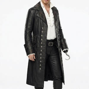 Puede incluir: Un abrigo largo de cuero negro con botones plateados y un pantalón de cuero negro a juego. El abrigo tiene un diseño largo y entallado con un cuello alto. El atuendo se completa con botas negras y un gancho plateado.