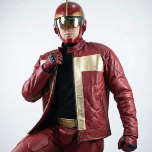 以下が含まれることがあります： 金色のアクセントが付いた赤い革のジャケットとパンツのセット、バイザー付きのお揃いのヘルメットと手袋。黒のタートルネックの上に着用。ジャケットはジッパー開閉式で、金色のベルトが付いています。