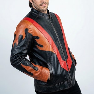K&ouml;nnte beinhalten: Schwarze Lederjacke mit orangefarbenem Flammendesign auf Schultern und &Auml;rmeln und einem roten Streifen auf der Vorderseite. Die Jacke hat einen Rei&szlig;verschluss und Taschen. Das Model tr&auml;gt eine schwarze Hose.