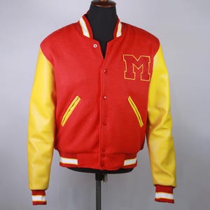 May include: A red and yellow varsity jacket with a large yellow "M" on the chest. The jacket has yellow leather sleeves, a red body, and white and yellow striped trim on the cuffs and waist. The jacket is buttoned up.