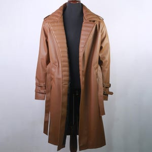 May include: A brown faux leather trench coat displayed on a mannequin. The coat features a notched collar, a double-breasted design, and a belt. The sleeves have buckle details, and the coat extends to the mid-calf.