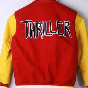 May include: Red and yellow varsity jacket with the word "THRILLER" in black and white lettering across the back. The jacket has yellow sleeves, a red body, and white and yellow striped trim.