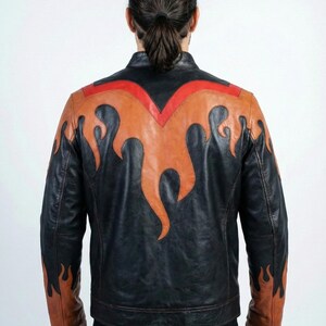 K&ouml;nnte beinhalten: Schwarze Lederjacke mit Flammendesign in Orange- und Rott&ouml;nen. Die Jacke hat einen klassischen Biker-Stil mit Stehkragen und taillierter Passform. Das Flammendesign befindet sich auf dem R&uuml;cken und den &Auml;rmeln.