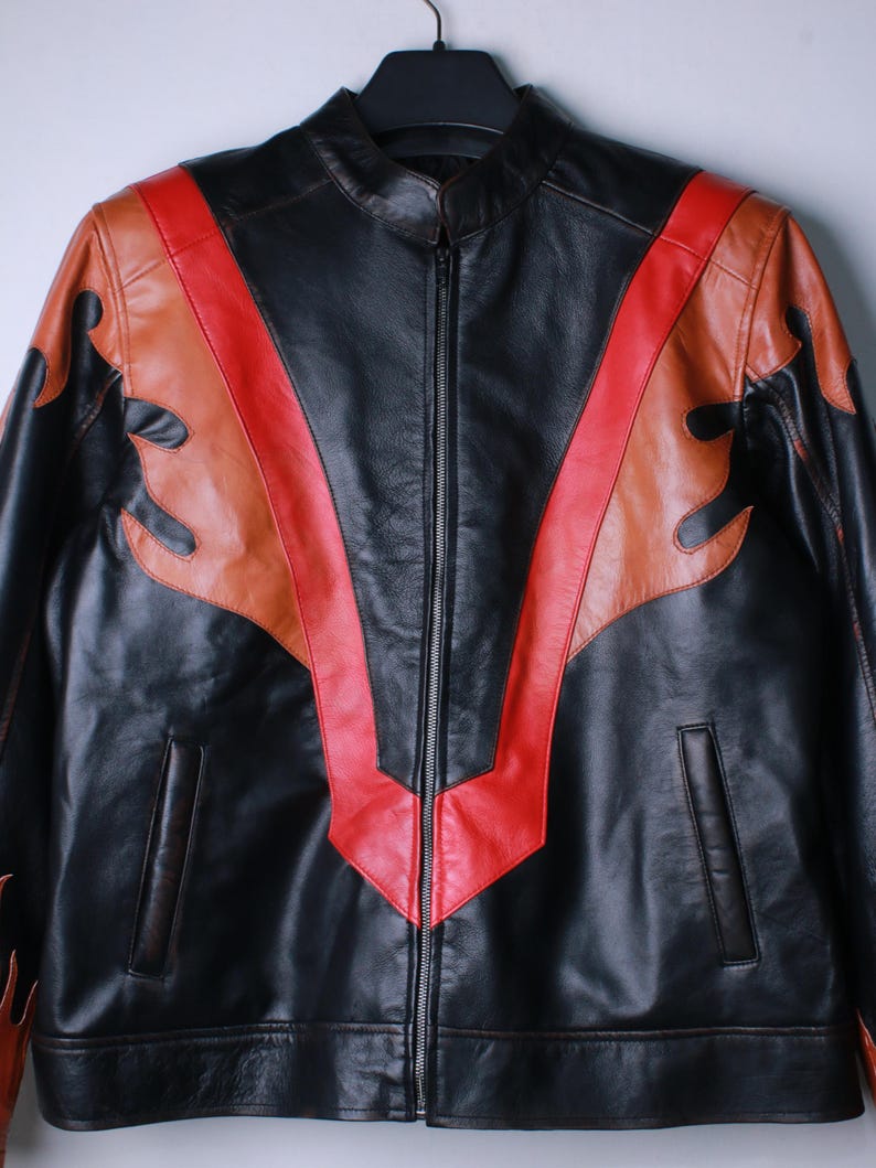 K&ouml;nnte beinhalten: Schwarze Lederjacke mit Stehkragen und durchgehendem Rei&szlig;verschluss. Die Jacke hat rote und braune flammenartige Designs auf den Schultern und der Brust. Die Jacke hat zwei Vordertaschen.