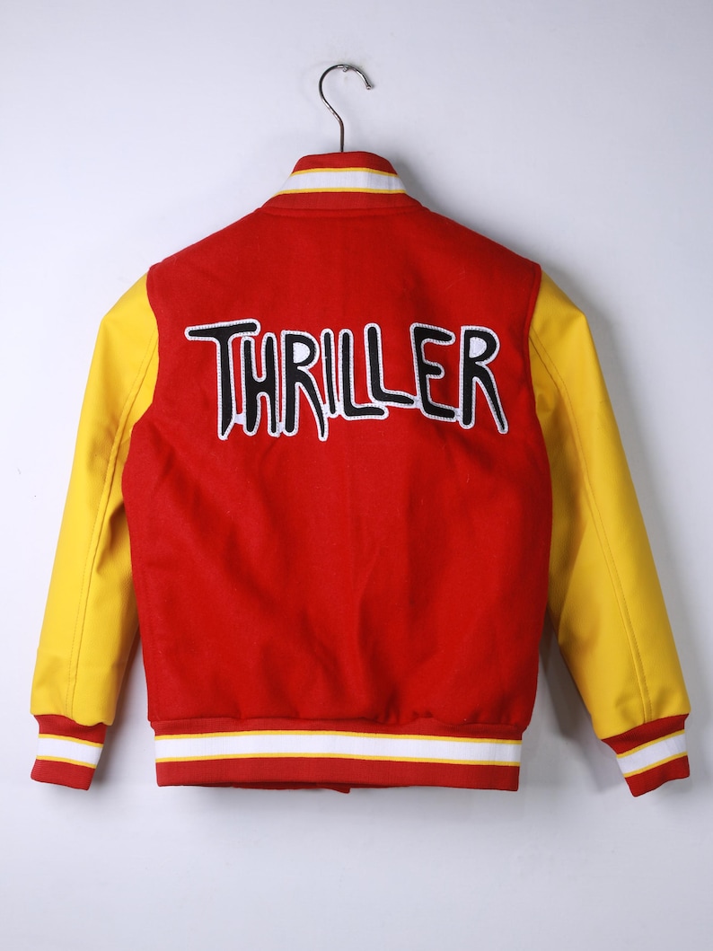 May include: Red and yellow varsity jacket with the word "THRILLER" embroidered on the back in black and white. The jacket has yellow sleeves, a red body, and white and red striped cuffs and collar.