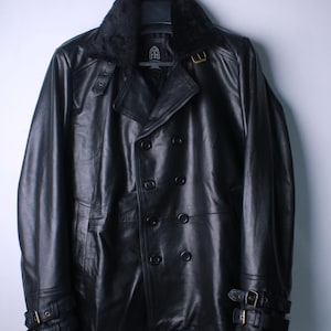May include: Black leather jacket with a faux fur collar, double-breasted front, and buckle details on the sleeves. The jacket is hanging on a hanger against a plain background. The jacket has a classic, timeless design.