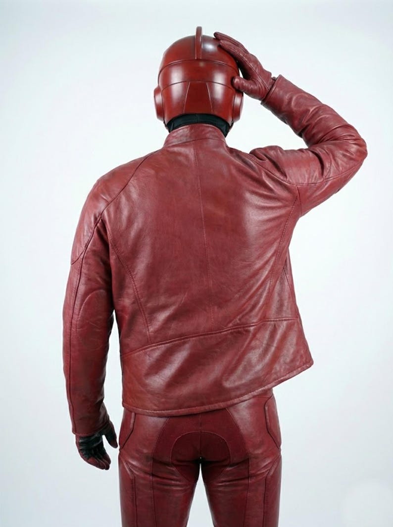 以下が含まれることがあります： 赤い革のジャケット、パンツ、手袋、ヘルメットを着用した人物。 衣装は濃い赤色です。人物はカメラから背を向けており、頭に手を置いています。