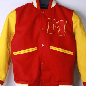May include: A red and yellow varsity jacket with the letter "M" embroidered on the chest. The jacket features yellow sleeves, a white and yellow striped collar, and white and yellow striped cuffs. The jacket has two front pockets and a button-up closure.