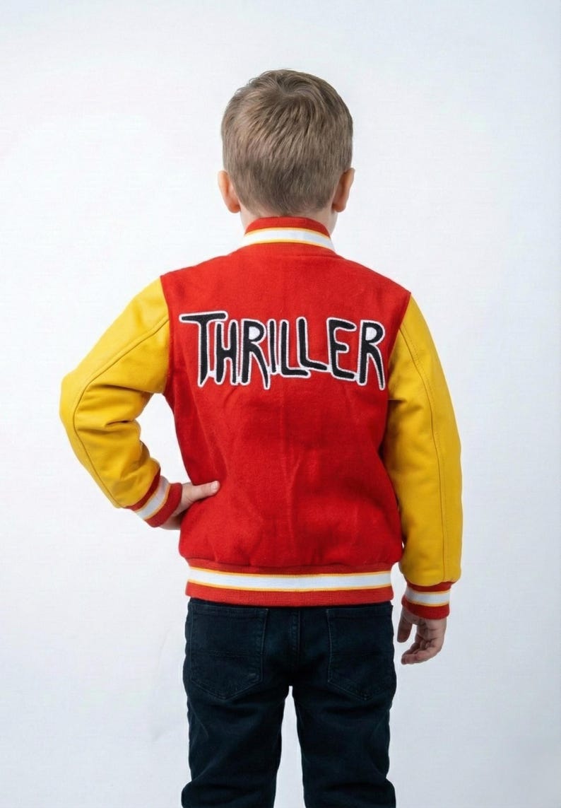 May include: Red and yellow varsity jacket with the word "THRILLER" in black and white lettering on the back. The jacket has yellow sleeves, a red body, and white and black striped trim. The jacket is worn with dark blue jeans.