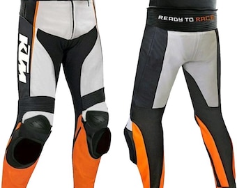 May include: Motorcycle racing pants in white, black, and orange. The pants feature knee protection and the KTM logo. The waist area is black, and the lower legs are orange. The pants are designed for racing and have a streamlined fit.