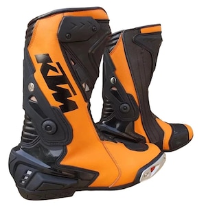 Puede incluir: Par de botas de moto naranjas y negras. Las botas presentan el logotipo de KTM en negro en el lateral. Están hechas de una combinación de cuero y materiales sintéticos, con zonas reforzadas para protección. Las suelas son plateadas y negras.