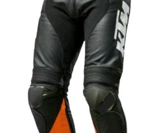 May include: Black and orange motorcycle pants with knee protection. The pants feature a black leather design with orange accents on the lower legs and waist. The KTM logo is visible on the side of the pants.