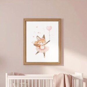 May include: A framed watercolor print of a dancing fox in a pink tutu holding a heart-shaped balloon. The artwork is in a gold frame and hangs above a white crib in a pink nursery. A teddy bear and ottoman are also in the room.