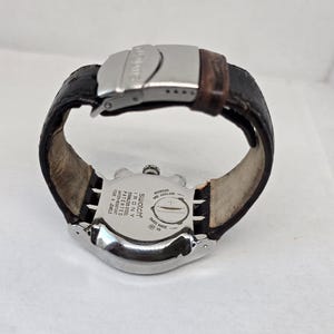 May include: A Swatch Irony stainless steel watch with a dark brown leather strap and a silver-tone metal deployment clasp. The back of the watch case features engraved text including Swatch Irony, stainless steel, patented, water-resistant, and four jewels.