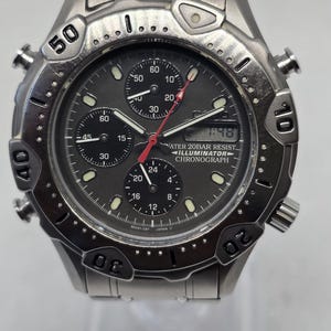 May include: A silver-toned stainless steel analog-digital wristwatch with a dark gray dial, three sub-dials, and a rotating bezel marked with numbers. The watch face features the text WATER 20BAR RESIST, ILLUMINATOR, and CHRONOGRAPH.