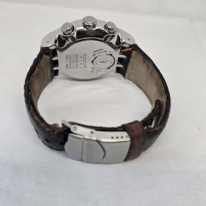 May include: A Swatch Irony stainless steel watch with a brown textured leather strap and a silver-tone metal deployment clasp. The back of the watch case features the text Swatch Irony, Stainless Steel, Patented, Water-Resistant, Four 4 Jewels.
