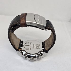 May include: A Swatch Irony wristwatch with a dark brown leather strap and a silver-tone metal deployment clasp. The stainless steel case back features the text Swatch Irony, Stainless Steel, Patented, Water-Resistant, and Four 4 Jewels.