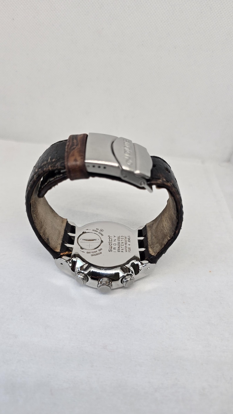 May include: A Swatch Irony wristwatch with a dark brown leather strap and a silver-tone metal deployment clasp. The stainless steel case back features the text Swatch Irony, Stainless Steel, Patented, Water-Resistant, and Four 4 Jewels.