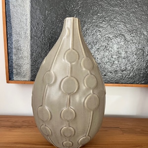 May include: A gray ceramic vase with a teardrop shape and a repeating pattern of circles connected by lines.