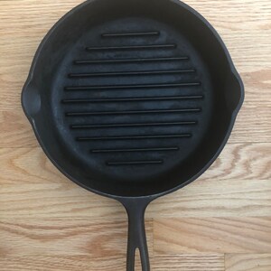 May include: A black cast iron grill pan with a long handle. The pan has a ridged surface for grilling.