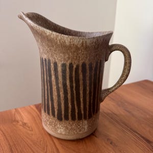 May include: A brown and black striped ceramic pitcher with a wide mouth and a handle. The pitcher has a speckled glaze.