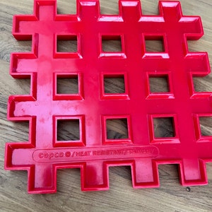 May include: Red plastic heat-resistant trivet with a grid pattern and the text "copco &copy;/HEAT RESISTANT/TAIWAN/" printed on the bottom.