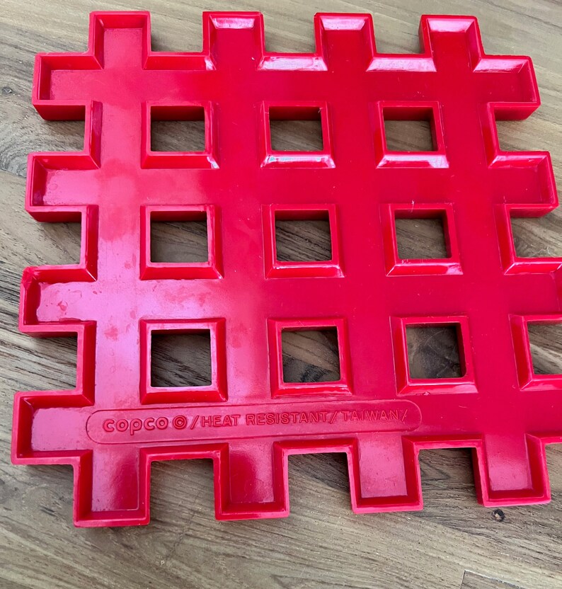 May include: Red plastic heat-resistant trivet with a grid pattern and the text "copco &copy;/HEAT RESISTANT/TAIWAN/" printed on the bottom.