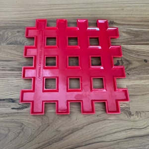 May include: A bright red plastic grid with square holes. The grid is made of interlocking pieces and has the text "Copyright 1983/1987/Taiwan" printed on the side.