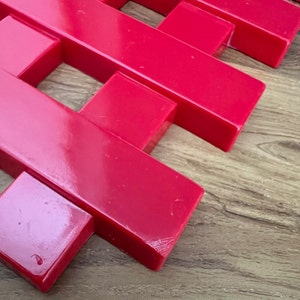 May include: A red plastic grid made of interlocking pieces. The grid is made of rectangular pieces that are connected to form a square pattern.