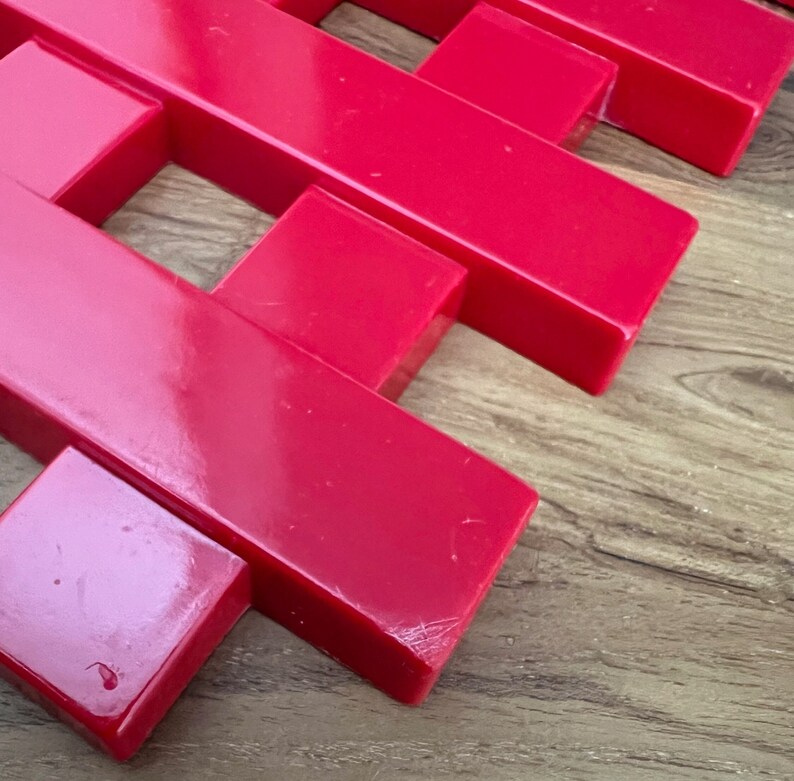 May include: A red plastic grid made of interlocking pieces. The grid is made of rectangular pieces that are connected to form a square pattern.