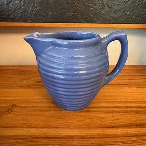 May include: A blue ceramic pitcher with a ribbed design. The pitcher has a wide mouth and a handle.