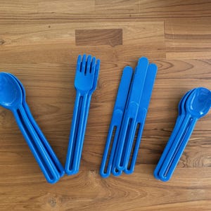 May include: A set of blue plastic utensils, including spoons, forks, and knives. The utensils are arranged on a wooden surface.