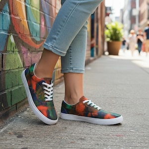 May include: Canvas trainers with a vibrant abstract pattern in orange, green, and blue. The shoes feature white laces and soles. The trainers are worn by a person standing on a pavement.
