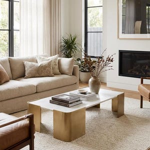 Peut inclure: Salon avec un canapé beige, des coussins décoratifs et une table basse avec un plateau en marbre et des pieds dorés. La pièce comprend une cheminée, de grandes fenêtres et un tapis neutre.