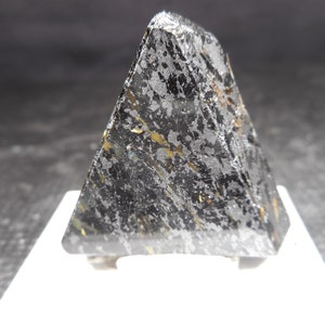 May include: A black, triangular shaped mineral specimen with gold and silver flecks. The mineral is on a white display stand.