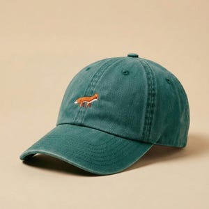 Op de afbeelding: Een teal baseball cap met een gebogen klep en een kleine, geborduurde vos in oranje en wit op de voorkant. De cap heeft een klassiek zes-panelen ontwerp met een bovenste knoop en een verstelbare band.