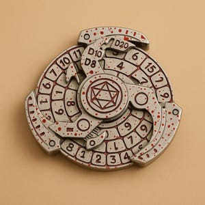 May include: A silver-colored, three-part fidget spinner with red accents and numbers. The spinner features dice symbols and numbers from 1 to 20, with D8, D10, and D20 markings. The design includes a central geometric shape.