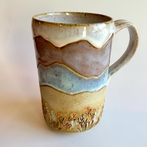 Peut inclure: Mug en céramique fait à la main avec un design en couches unique dans les tons de marron, bleu et beige. La tasse a une anse et un motif floral à la base. Une pièce fonctionnelle et décorative pour savourer des boissons.