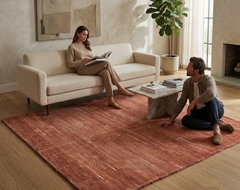 May include: A large rectangular area rug in a deep terracotta orange hue with subtle, light-colored horizontal striations and a textured pile. The rug is positioned on a light wood floor, featuring the Loom brand logo in the bottom right corner.