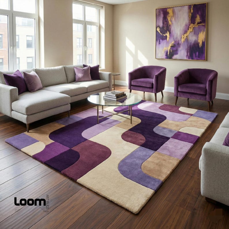 Puede incluir: Un sal&oacute;n moderno con un sof&aacute; esquinero gris, dos sillones morados y una alfombra estampada en tonos morados, beige y marr&oacute;n. Una mesa de centro redonda de cristal y una pintura abstracta completan la decoraci&oacute;n.