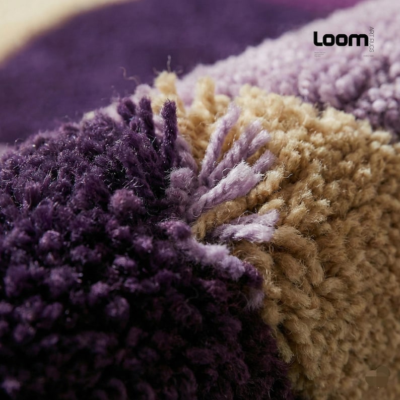 Puede incluir: Primer plano de una alfombra texturizada con un dise&ntilde;o de bloques de color. La alfombra presenta secciones de morado oscuro, morado claro y beige. Las fibras son gruesas y afelpadas, creando una apariencia suave y acogedora. La palabra "Loom" es visible.