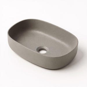 Può includere: Un lavabo in cemento grigio di forma ovale con bordi arrotondati. Il lavabo ha un singolo foro di scarico al centro e una finitura liscia e opaca. Il design è minimalista e moderno, adatto per un bagno.